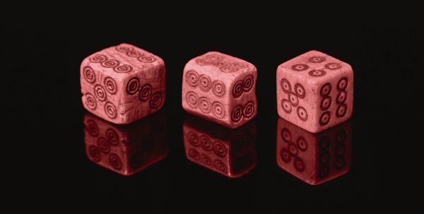 Three ancient dice sitting on a reflective surface.